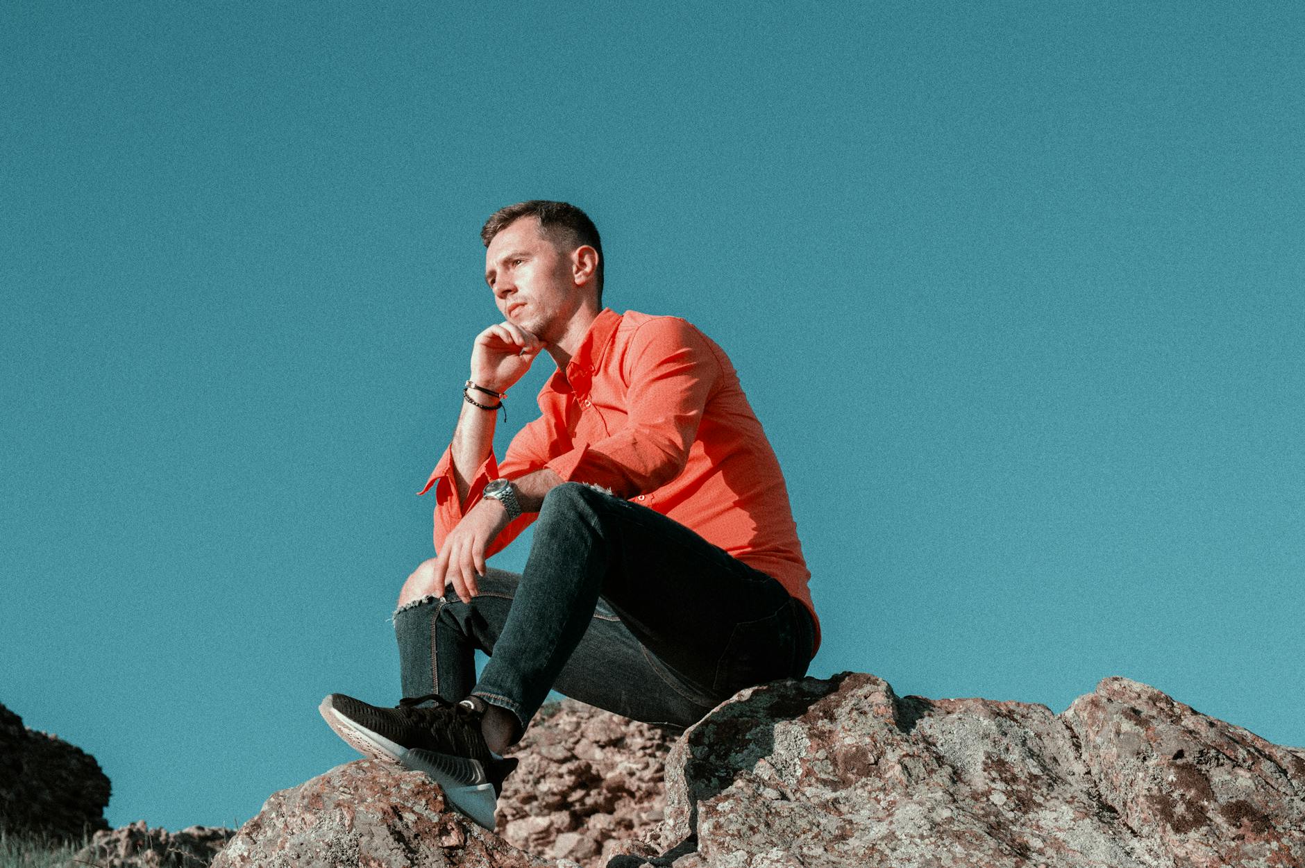 pensive man sitting on mountain peak